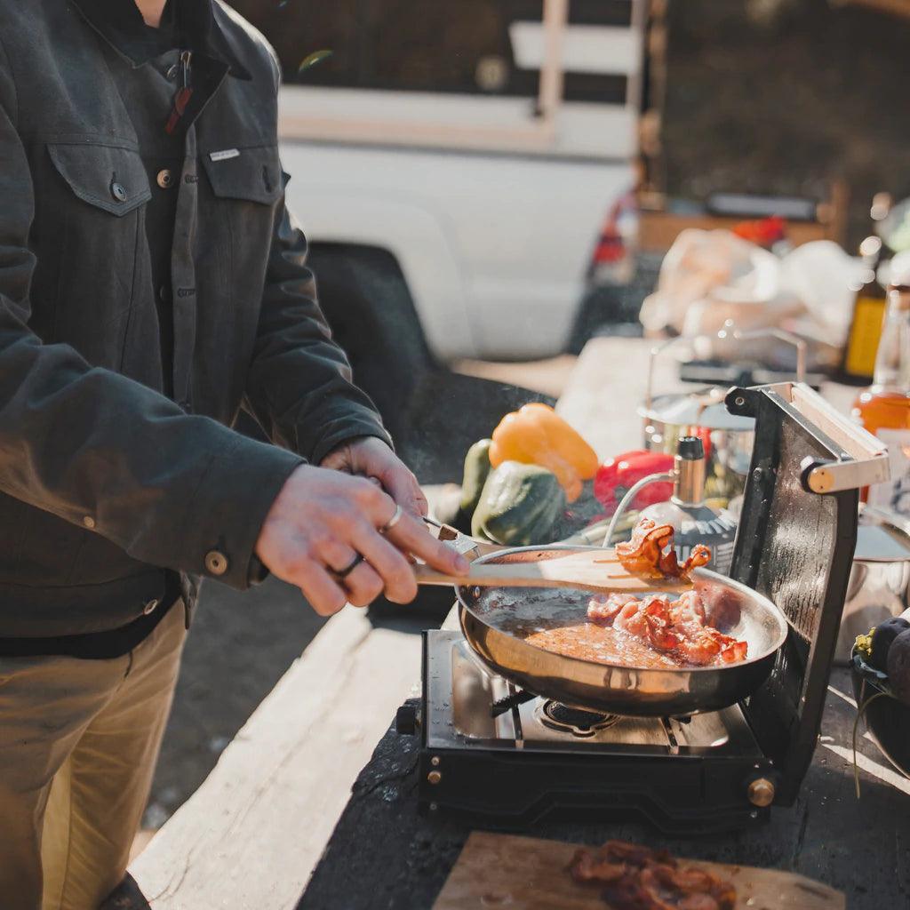 Cooking bacon on Primus Moja single burner camp stove outdoors at picnic table