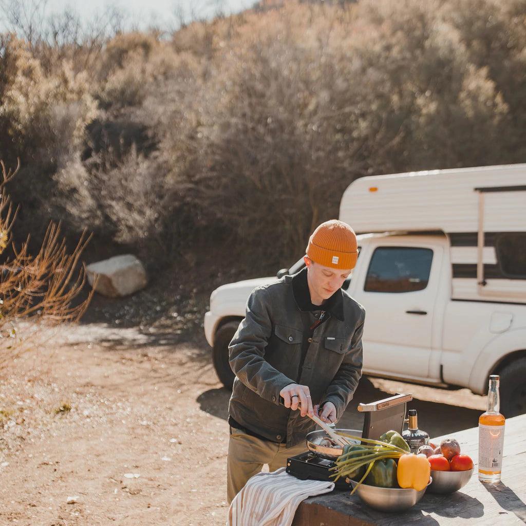 Man cooking with Primus Moja single-burner camp stove outdoors by white camper truck