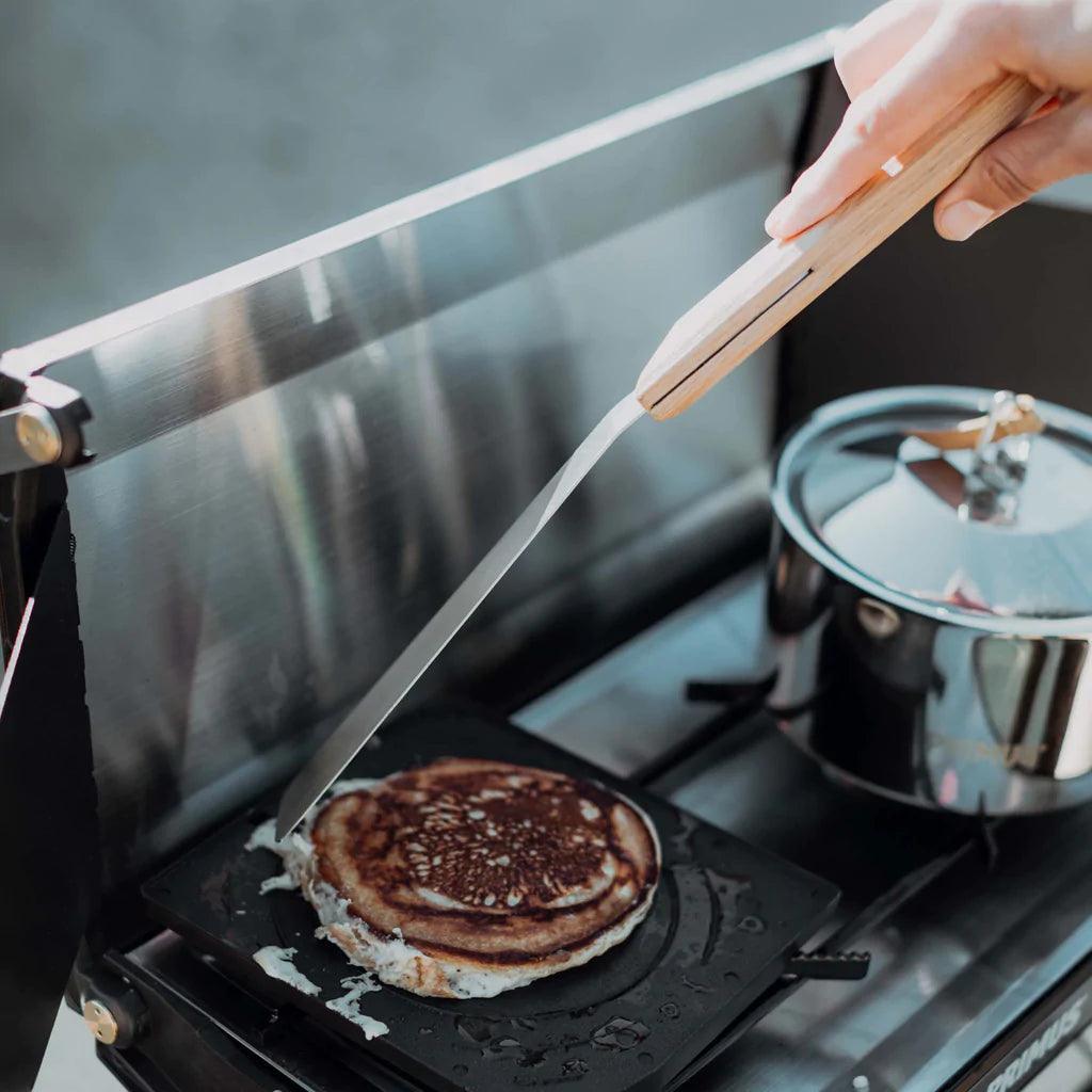 Hand flipping pancake with Primus OpenFire spatula on outdoor camping stove
