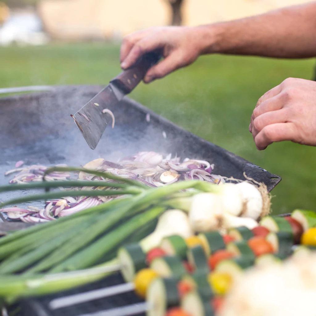 Hand using Primus Openfire spatula to grill onions and vegetables outdoors