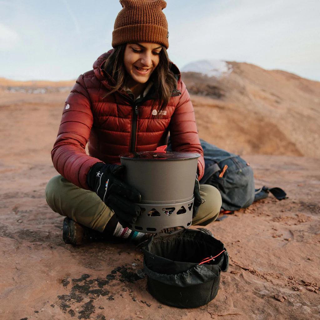 Woman using Primus PrimeTech stove system outdoors on rocky terrain