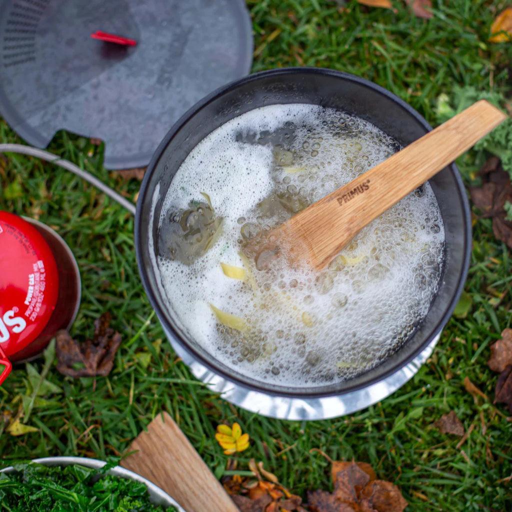 Primus stove system boiling food outdoors with wooden spatula on grass