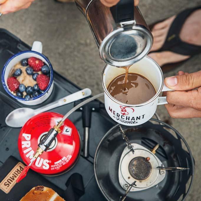 Primus camping stove with fuel canister, coffee pour, and berry oatmeal outdoors