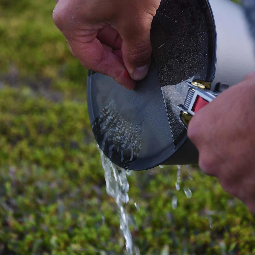 Hand straining water from camping pot with Primus PrimeTech stove system outdoors