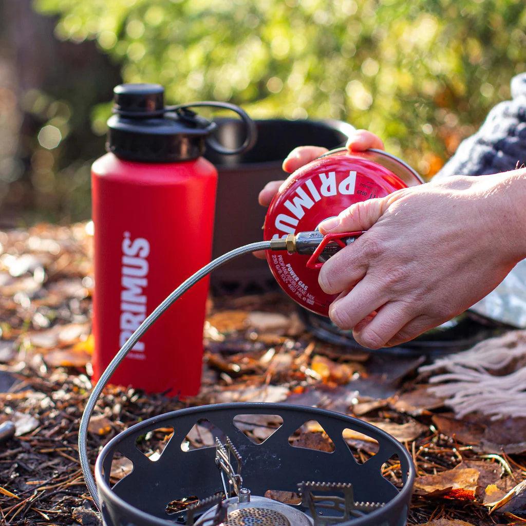 Primus stove system and red water bottle outdoors on forest floor during camping