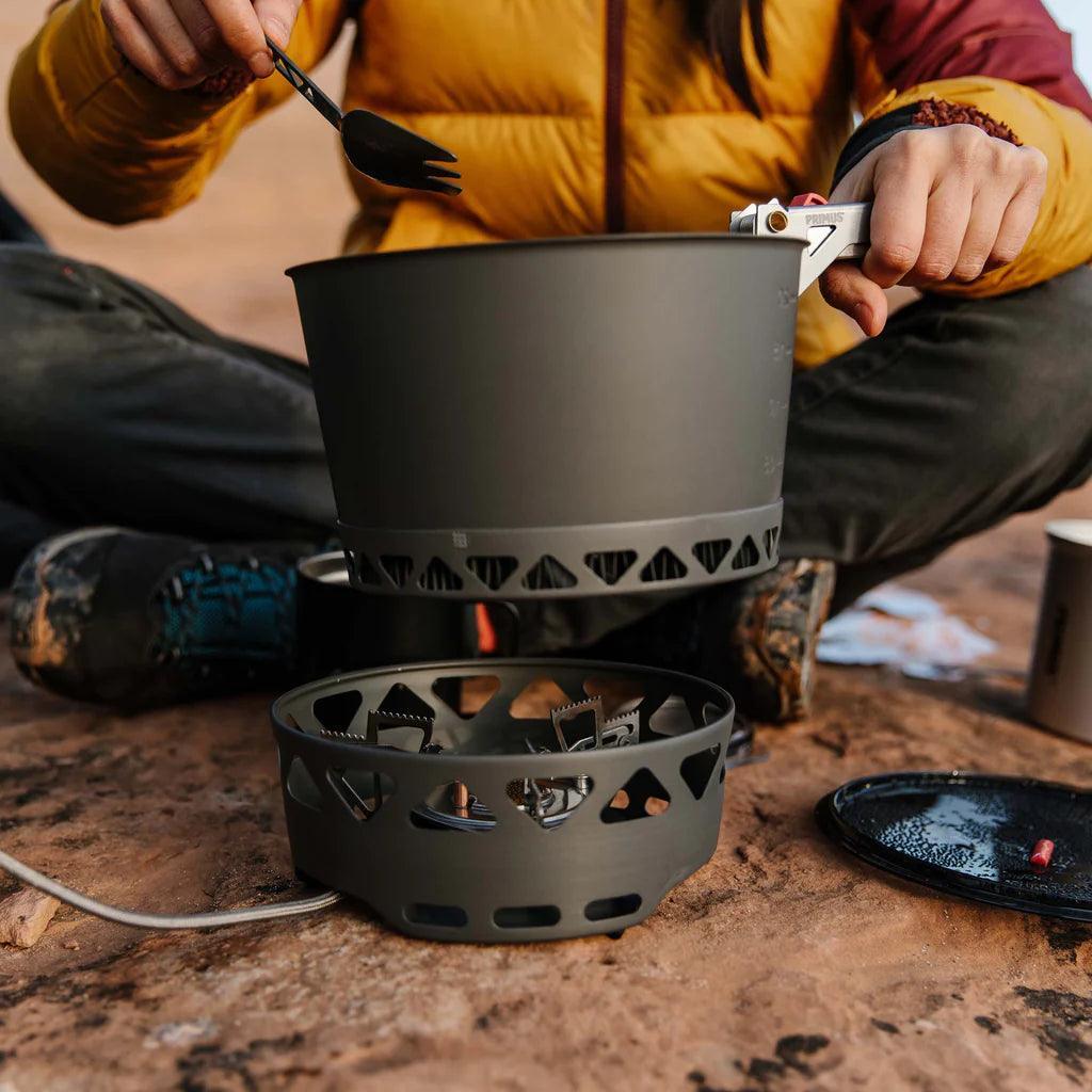 Primus PrimeTech stove system in use outdoors on rocky ground, camper in yellow jacket