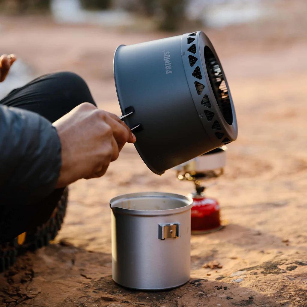 Person using Primus PrimeTech stove system outdoors on sandy ground