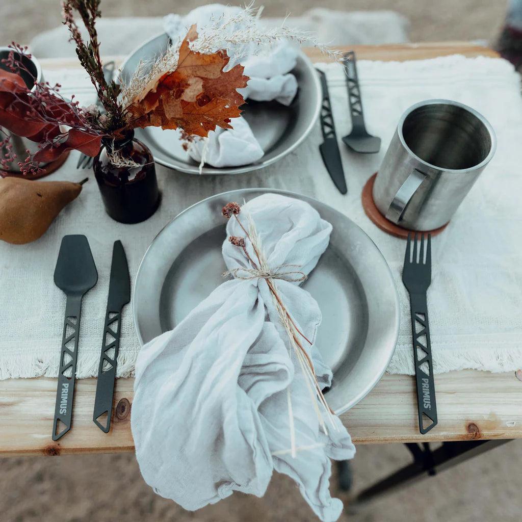 Primus aluminum camping cutlery set with plates, mug, and rustic outdoor table setup