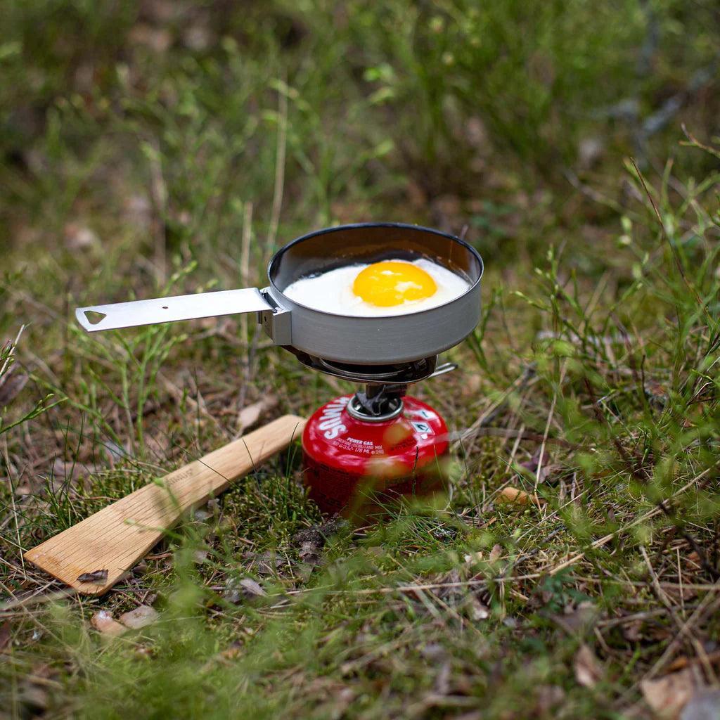 Camping stove with frying pan cooking egg outdoors in grass using Primus Trek Pots