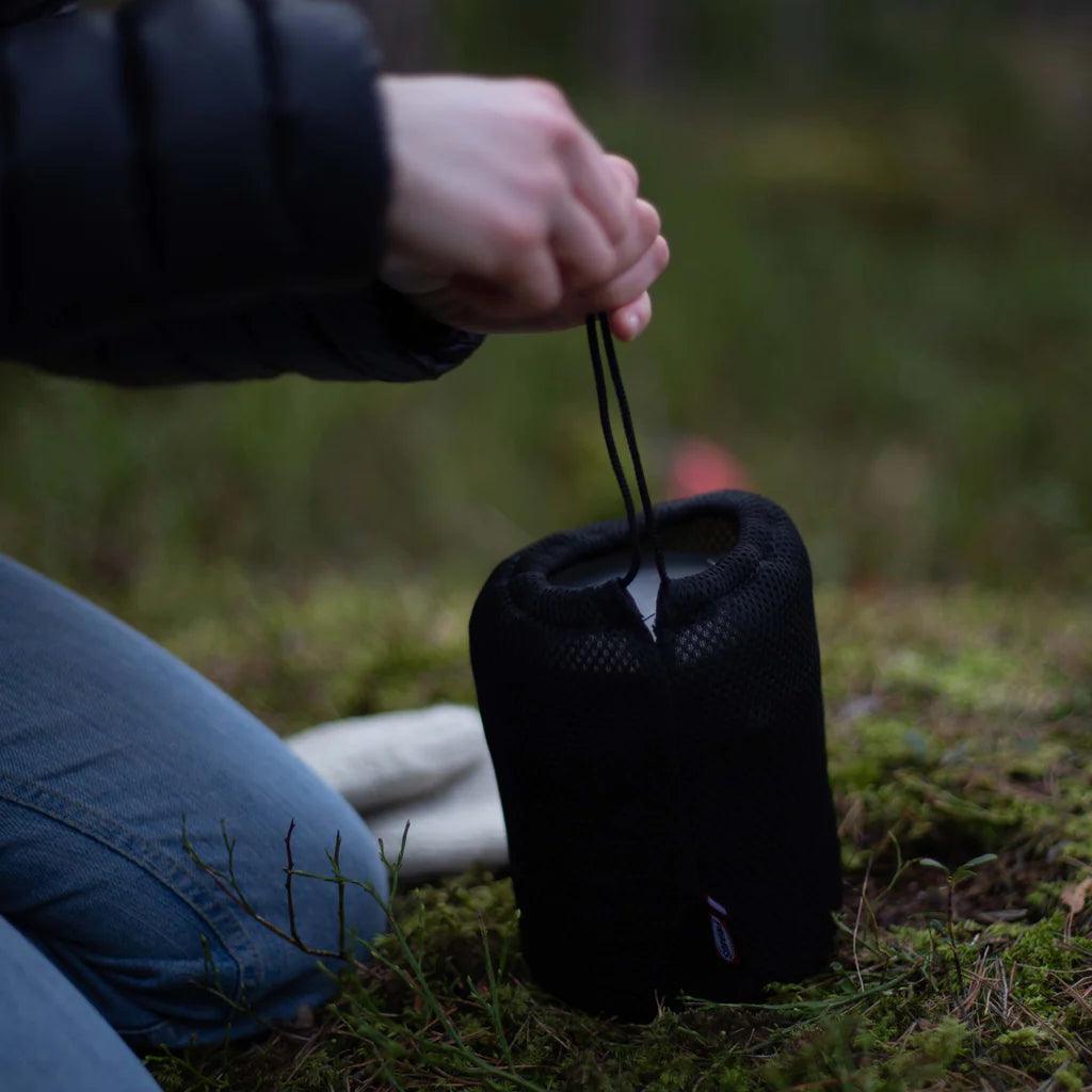 Person holding Primus Trek Pots in black mesh bag outdoors on forest ground