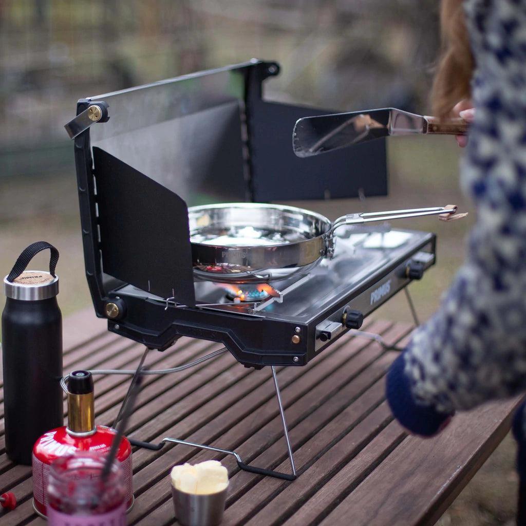 Primus Tupike camping stove on wooden table with pan and outdoor cooking gear