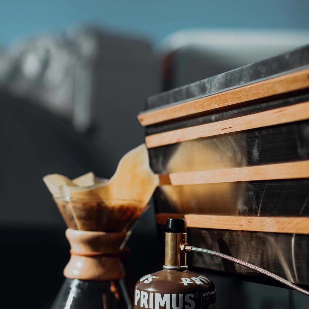 Primus Tupike stove and Primus fuel canister outdoors with Chemex coffee maker beside them