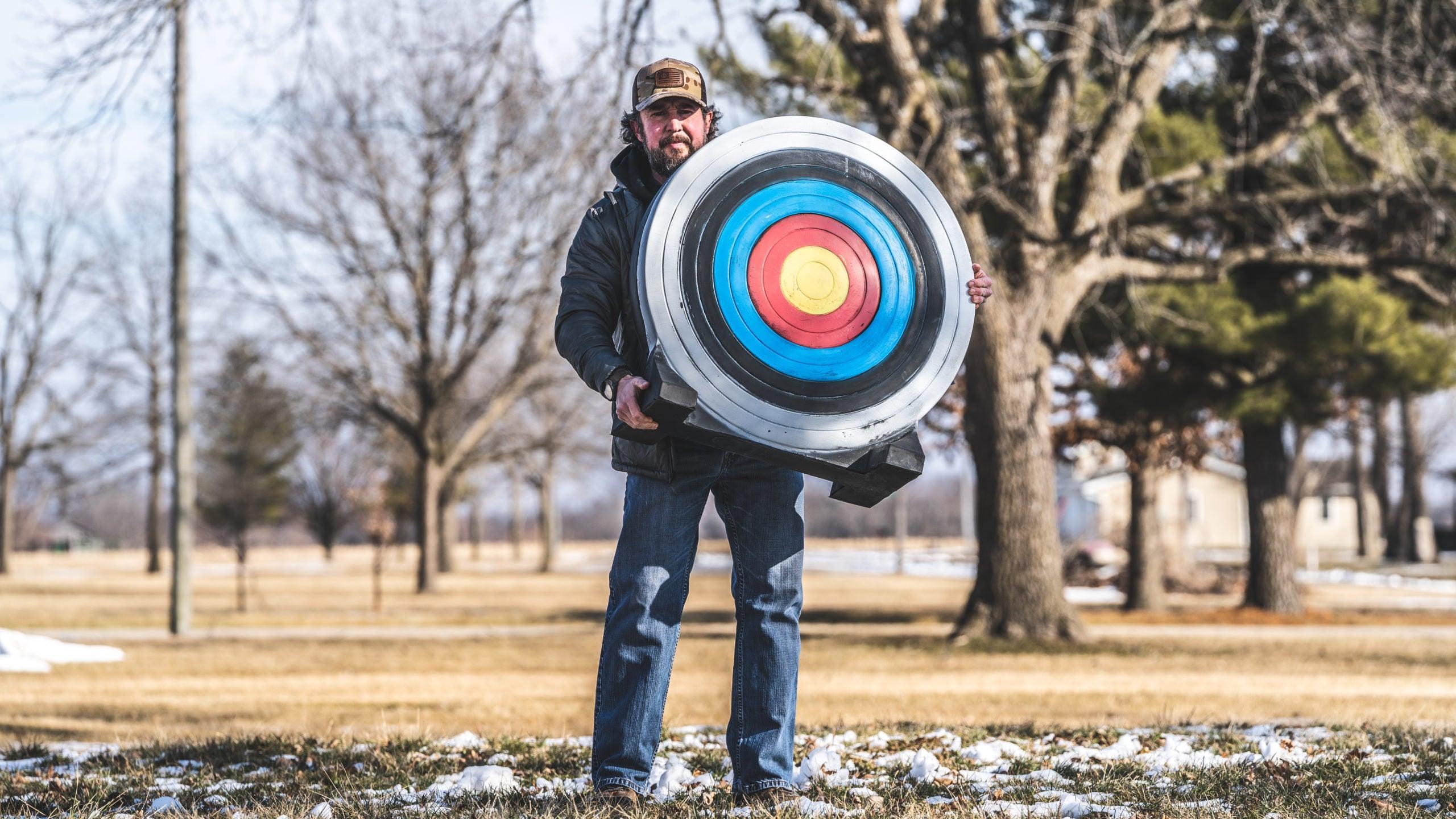 Man outdoors holding Rinehart Archery NASP target on snowy grass with trees in background