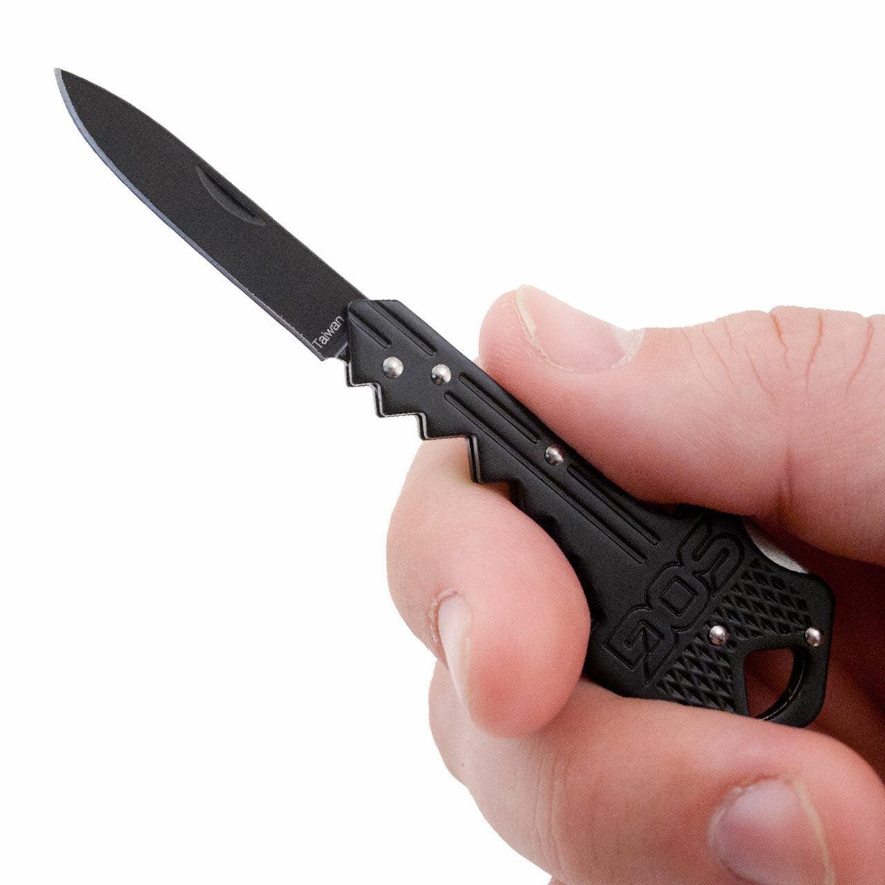 Hand holding SOG key knife with black blade and key-shaped handle on white background