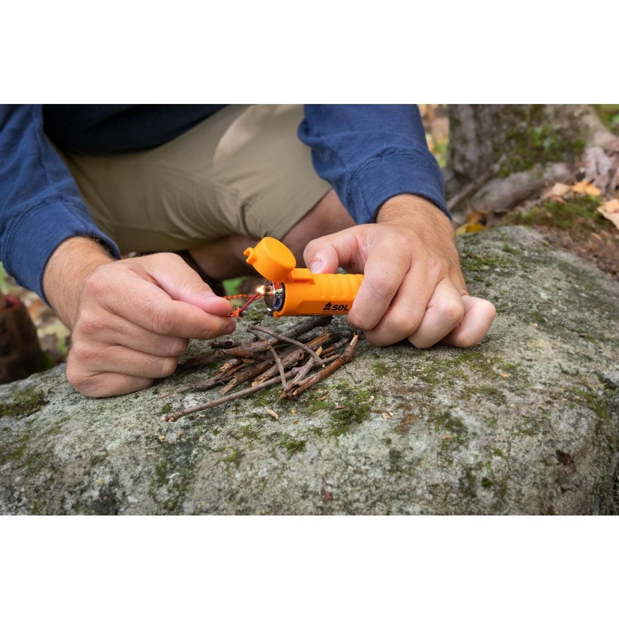 Person using orange SOL Fire Lite fuel-free lighter to ignite twigs on a rock outdoors