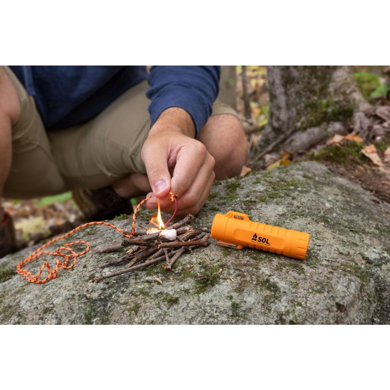 Person lighting campfire with SOL Fire Lite fuel-free lighter on a rock outdoors