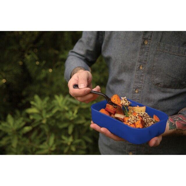 Person holding blue camping food container outdoors with vegetables and grains
