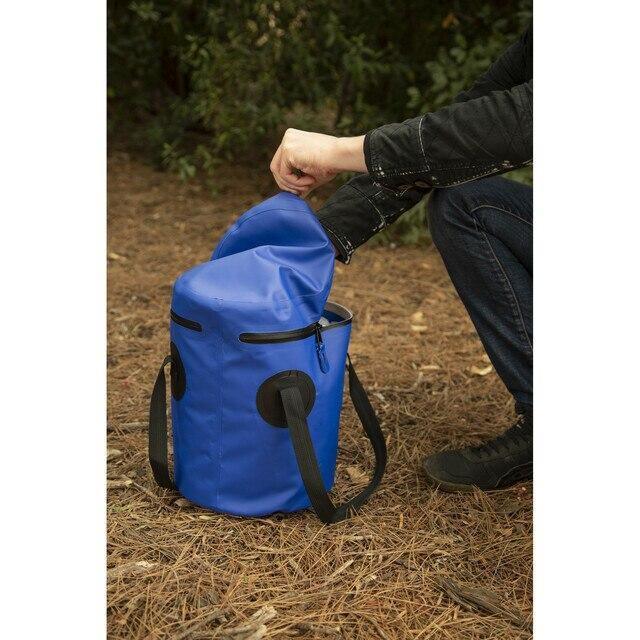 Person opening blue Stansport 12-liter outdoor trail bucket with lid in forest setting