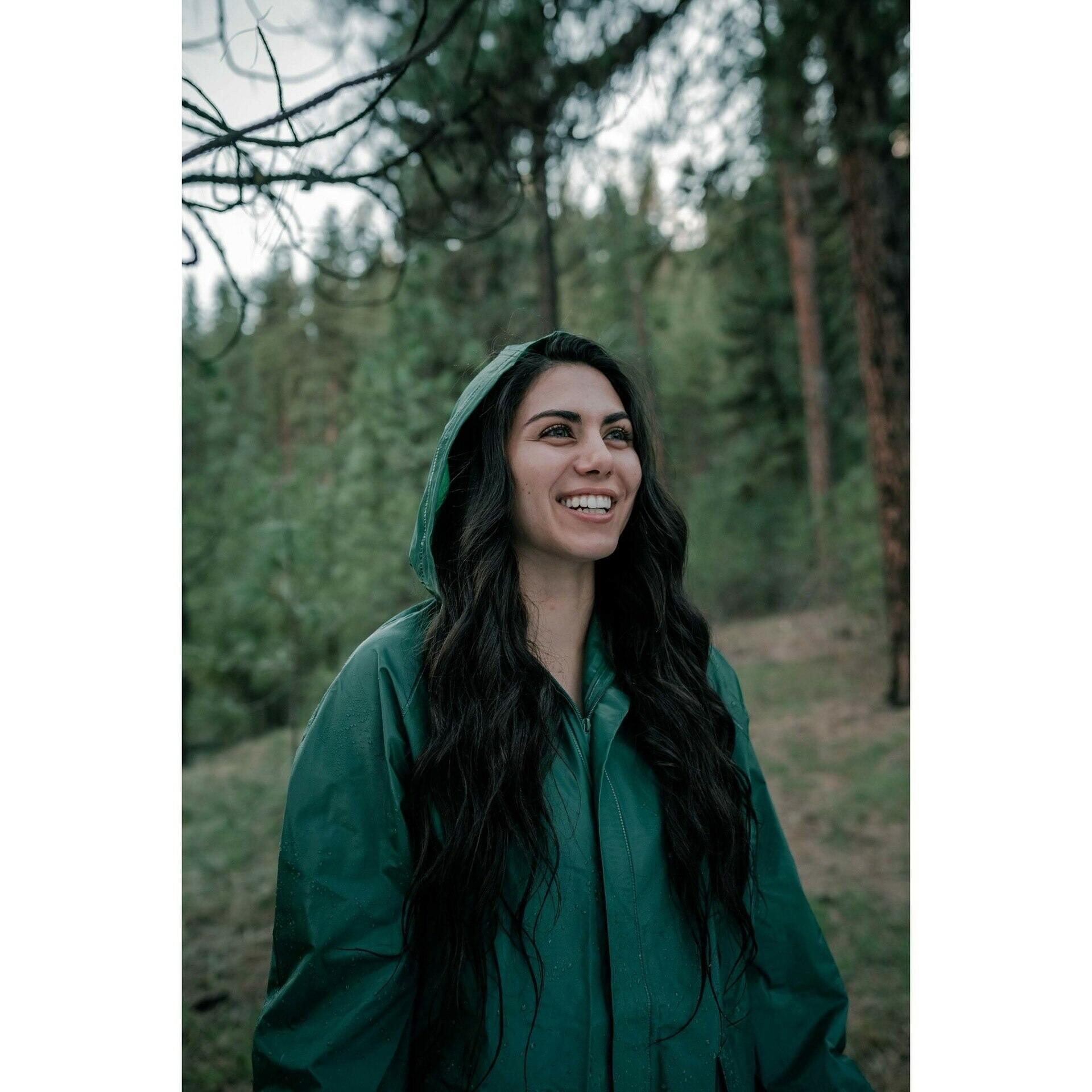 Woman wearing green rain suit jacket in a forest outdoors, smiling
