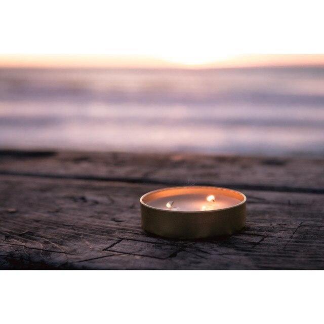 Three-wick survival candle on rustic wood near water at sunset, outdoor camping gear