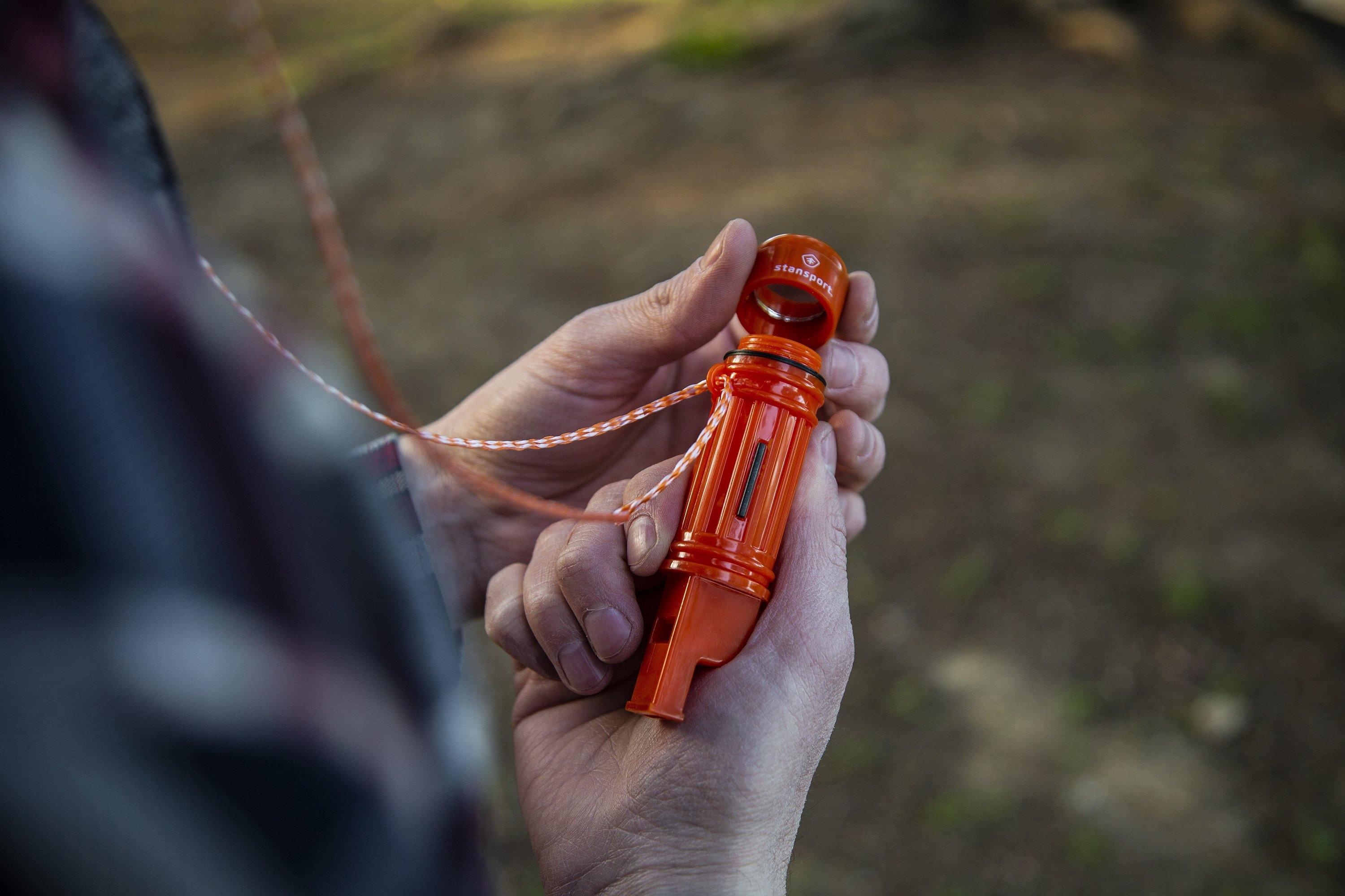 Hands holding orange Stansport 5-in-1 survival whistle outdoors with lanyard