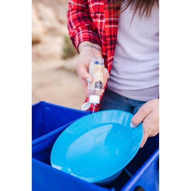 Person pouring Stansport all-purpose camper's soap onto blue camping dish outdoors
