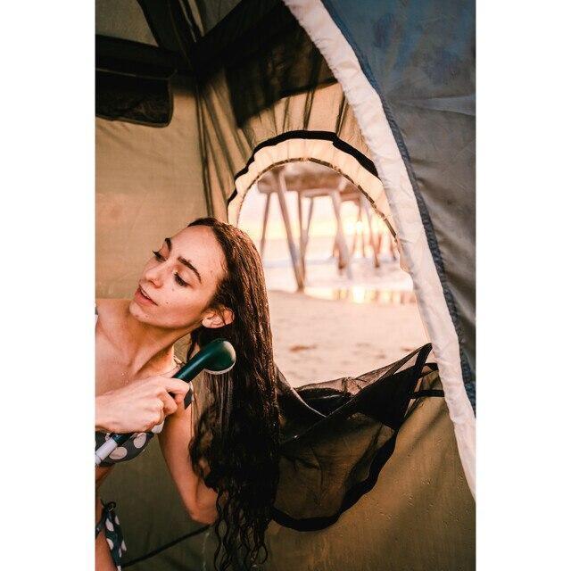 Woman using portable battery-powered shower inside beach tent at sunset