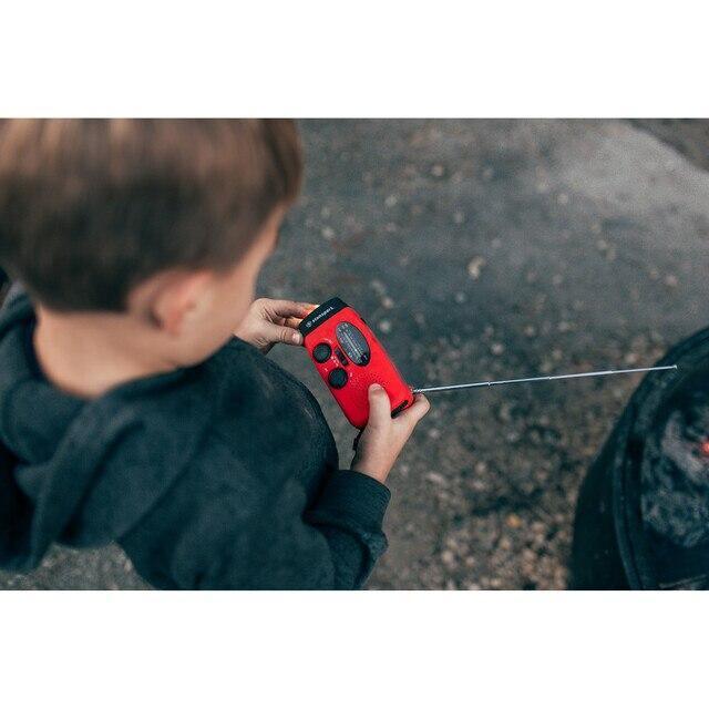 Child holding red handheld solar dynamo flashlight radio outdoors