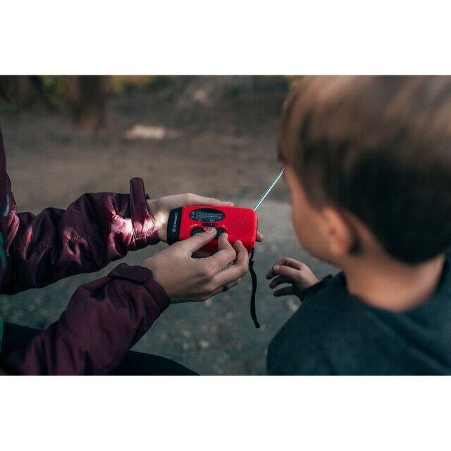 Adult showing child a red handheld solar dynamo flashlight radio outdoors