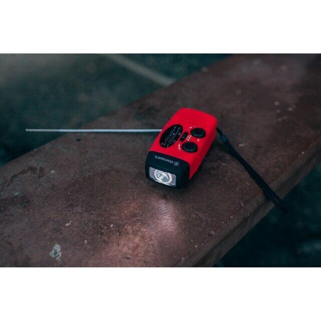 Red Stansport handheld solar dynamo flashlight radio on a brown outdoor bench