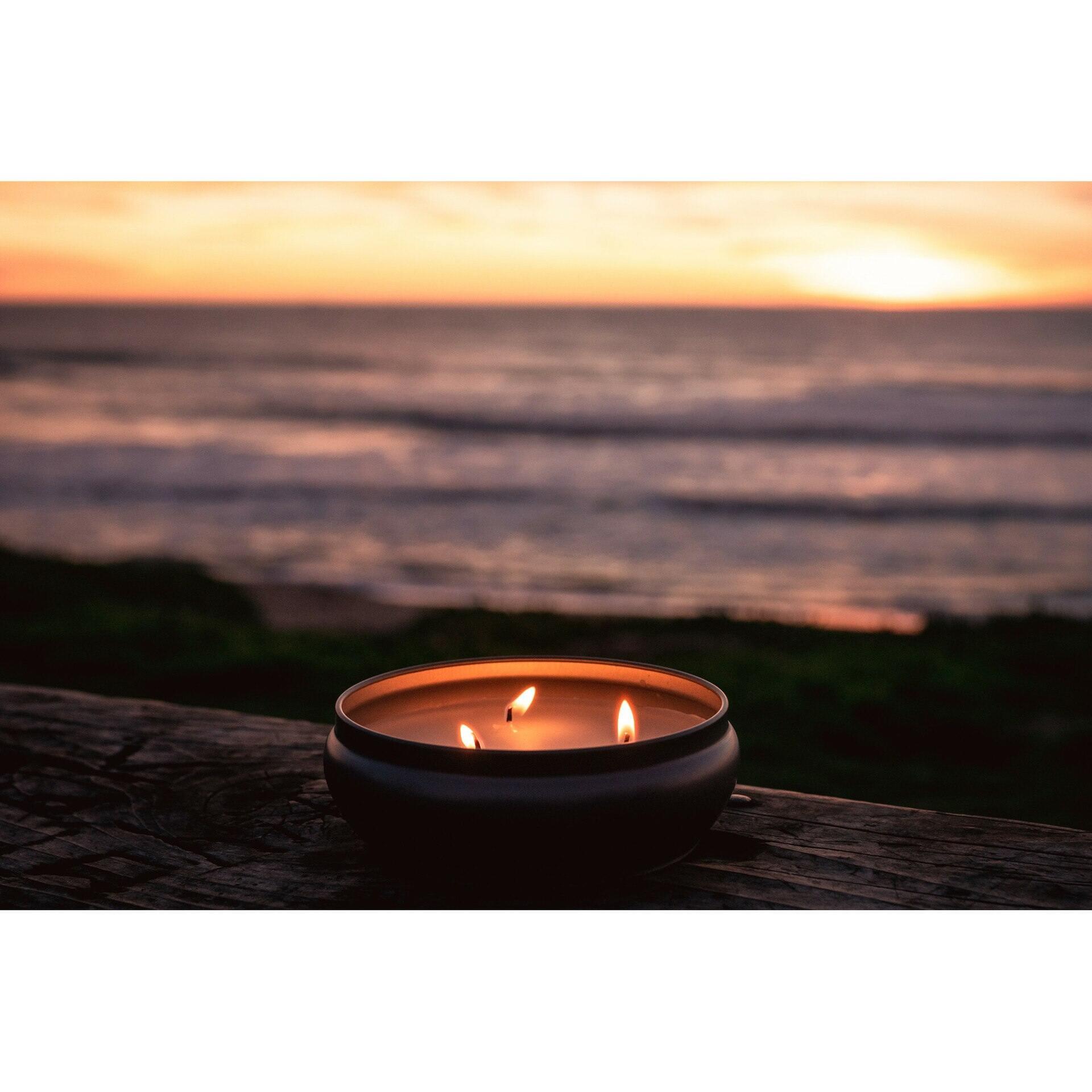 Citronella insect repellent candle with three wicks on a wooden surface by the beach at sunset