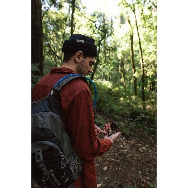 Man hiking in forest with backpack using Stansport lensatic compass