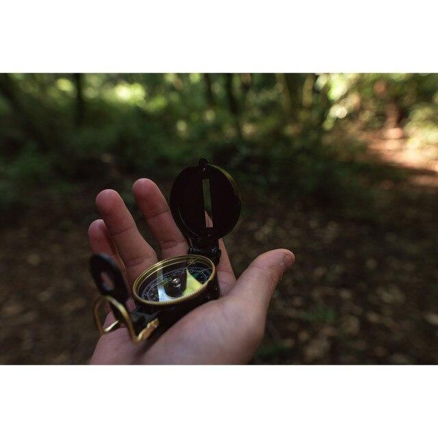 Hand holding a Stansport lensatic metal compass in a forest, outdoor navigation gear