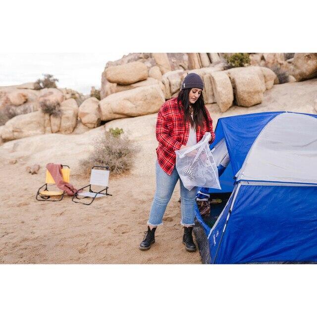 Woman at campsite holding mesh laundry bag by blue tent with rocks in background