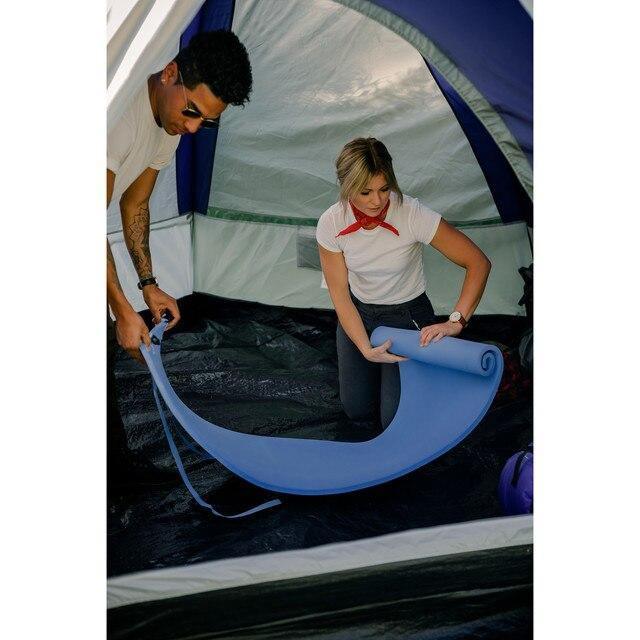 Two people rolling out a blue camping sleeping pad inside a tent