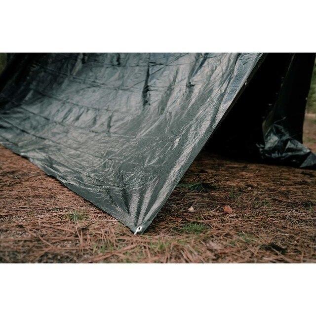 Green rip-stop tarp set up outdoors on pine needles, durable camping shelter