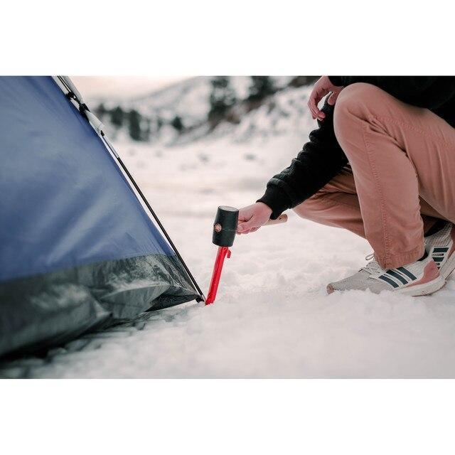 Person using a rubber mallet to secure a tent peg in snow during winter camping