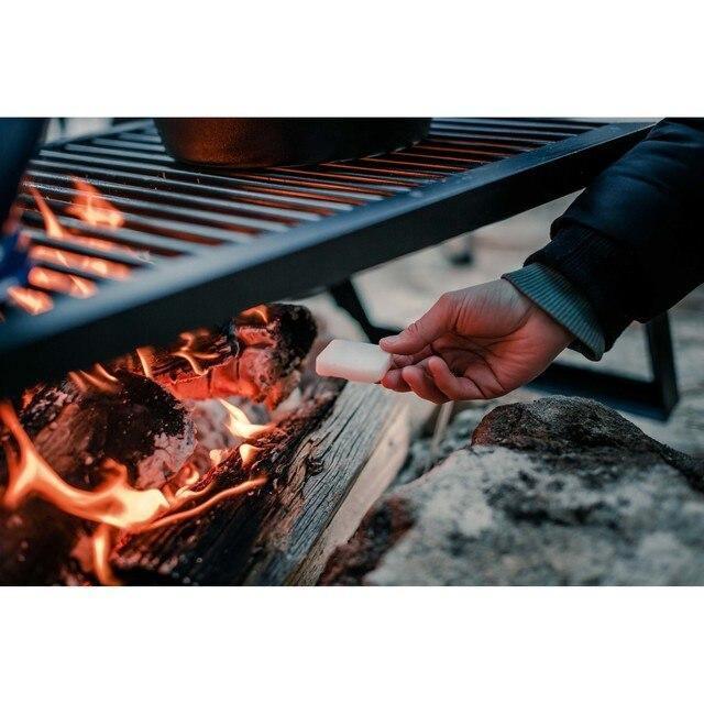 Hand placing solid fuel tablet into campfire under outdoor grill