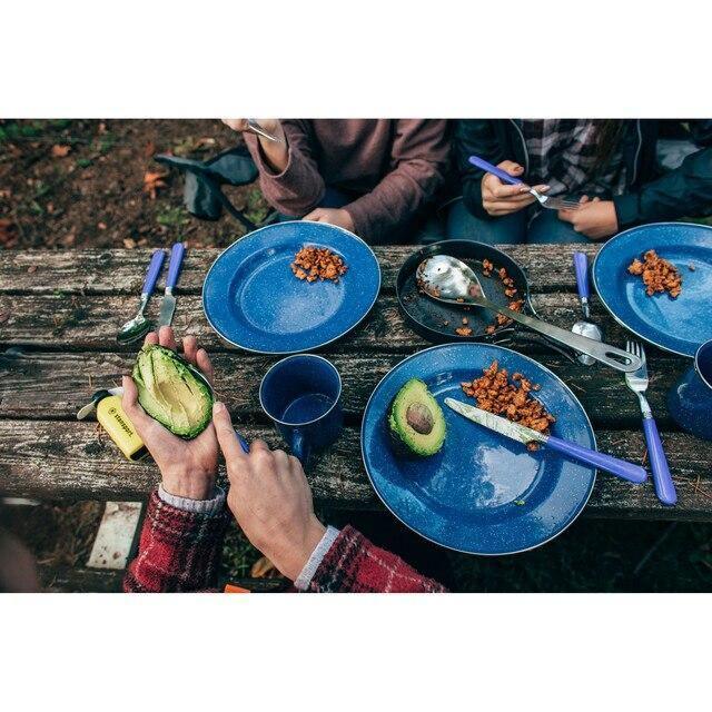 Outdoor camping meal with blue plates, utensils, avocado, and food on rustic picnic table