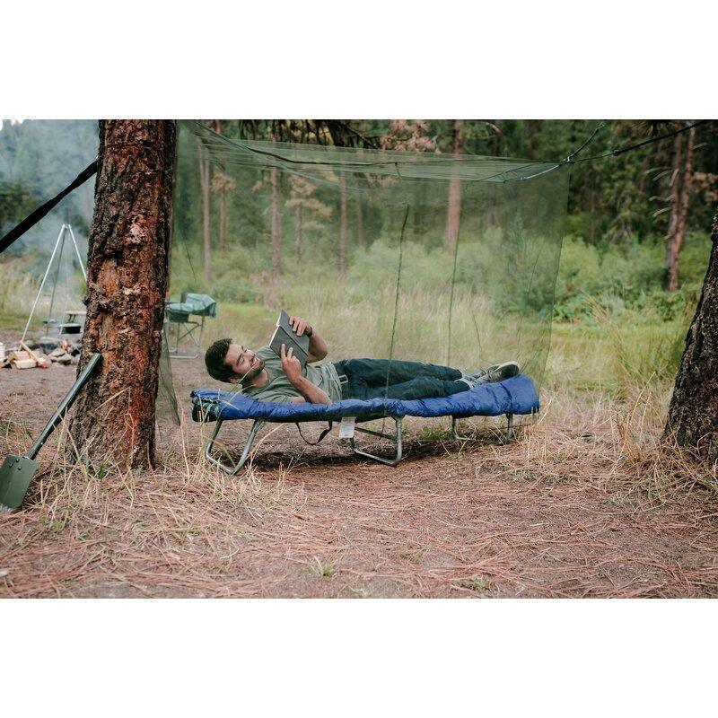 Man relaxing on a camping cot under suspension mosquito netting in a forest campsite