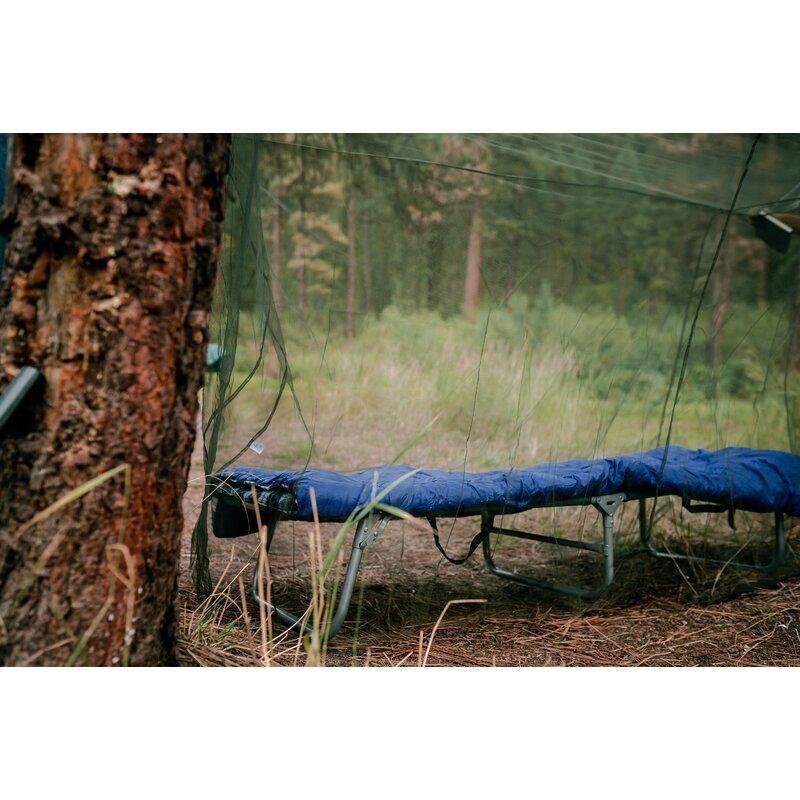 Camping cot under mosquito netting in forest with sleeping bag