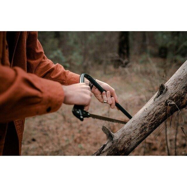 Person using a steel bow saw to cut a tree branch outdoors in the forest