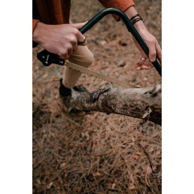 Person using a steel bow saw to cut a tree branch outdoors on forest ground