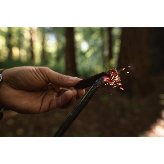 Hand lighting a Stansport wood charcoal fuel stick with sparks in a forest setting