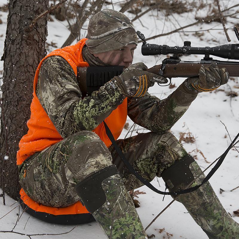 Hunter in camouflage and orange vest aiming rifle in snowy woods using Thermaseat Heat-A-Seat.