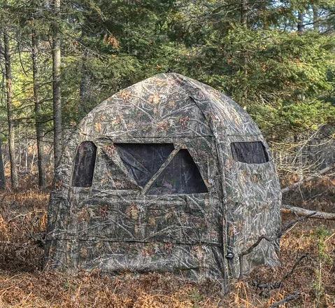 Camouflage inflatable ground blind set up in a forest for hunting or outdoor sports.