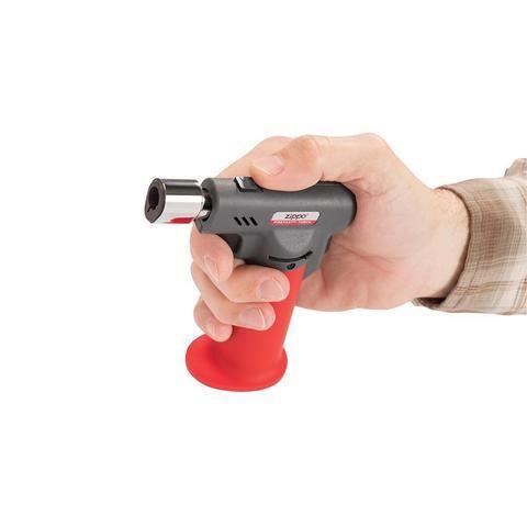 Hand holding Zippo FireFast torch with red grip on white background