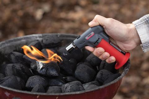 Hand using Zippo FireFast torch to light charcoal in outdoor barbecue grill