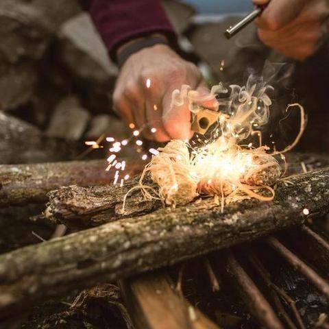Hand igniting Zippo Tinder Shreds with fire starter on wood outdoors