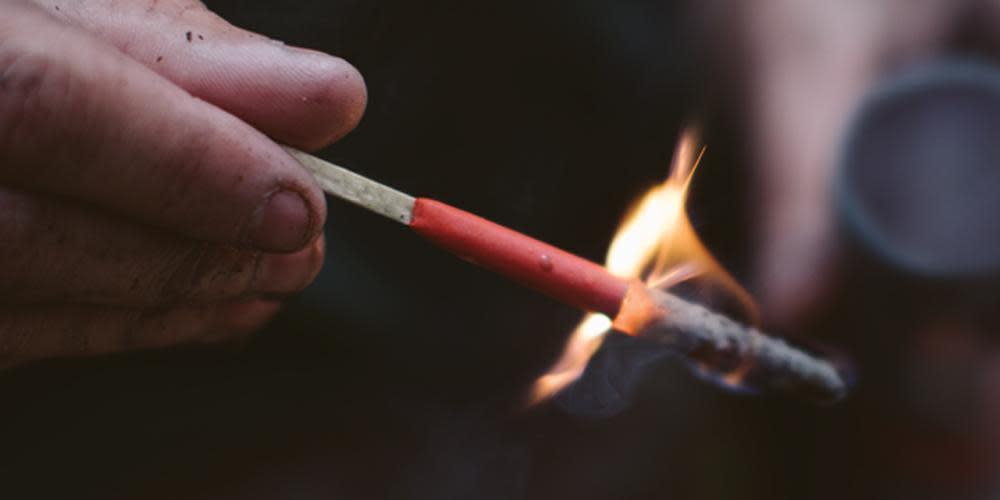 Hand holding lit Zippo Typhoon match with orange tip and flame outdoors